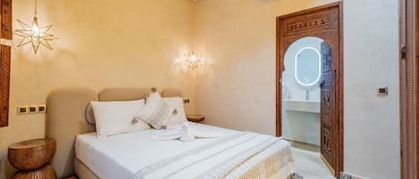 A bedroom with a bed, bedside tables, a hanging light fixture, a wall-mounted air conditioner, and a wooden door with a mirror.