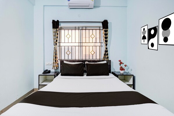 Habitación de hotel con cama, mesita de noche con teléfono, aire acondicionado de pared y ventana con cortinas decorativas.