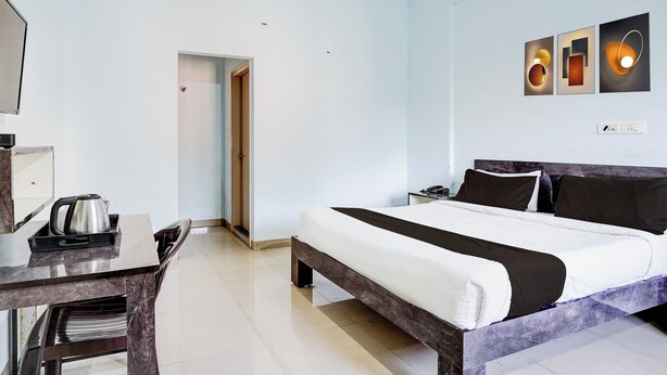 A hotel room with a bed, a desk with a kettle, a nightstand, and a wall with three framed pictures. - Super Collection O Uttarahalli (Bangalore)