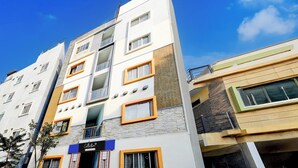 A multi-story building with a modern architectural design, featuring a mix of window styles and a visible storefront with signage. - Super Collection O Uttarahalli (Bangalore)