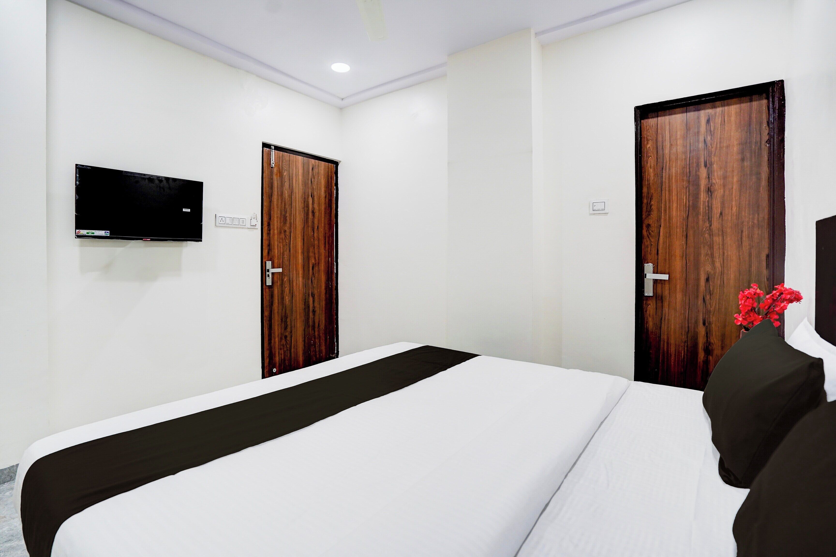 A hotel room with a bed, a television mounted on the wall, and two wooden doors.