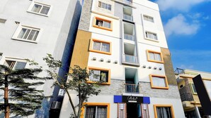 A multi-story building with a modern architectural design, featuring a mix of white and beige facades, and a prominent blue sign indicating a company service. - Super Collection O Uttarahalli (Bangalore)