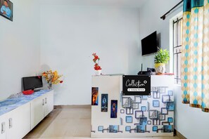 Un área de recepción con un mostrador, un televisor de pantalla plana, un jarrón con flores y un letrero que dice 'Collection Company Serviced'.