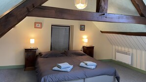A bedroom with a sloped ceiling, a bed with a headboard, two bedside lamps, and a window with a patterned curtain. - Gîte "Le Faisan" with Private Terrace, Enclosed Garden, and Wifi (Audes)
