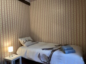 Un dormitorio con cama, almohadas, lámpara de noche y pared a rayas verticales.