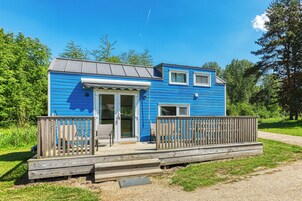 Una cabaña azul pequeña con terraza de madera, una puerta y un ventanal.