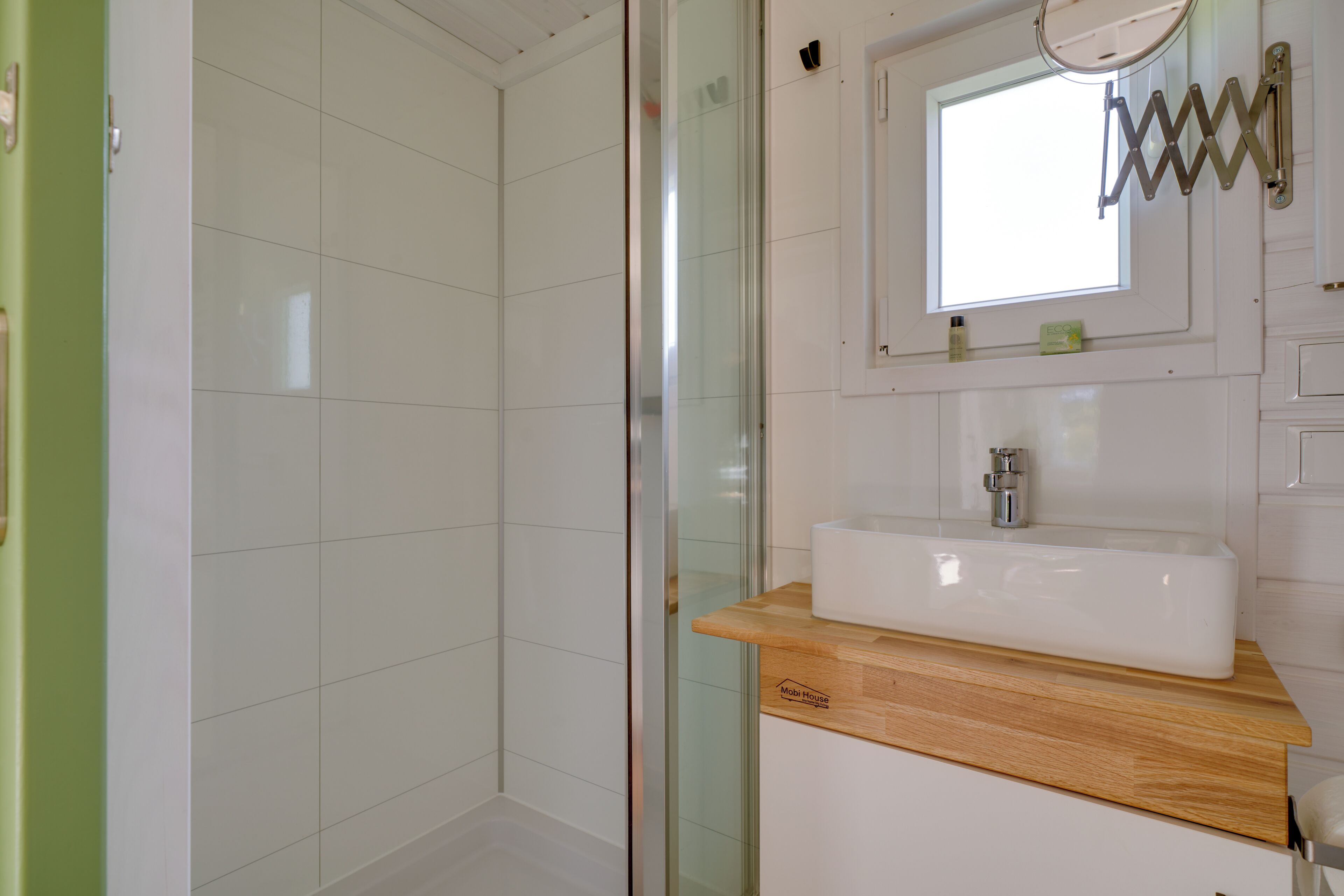 Un baño con cabina de ducha de vidrio, un lavamanos blanco con encimera de madera y un espejo con marco metálico.