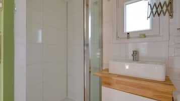 Un baño con cabina de ducha de vidrio, un lavamanos blanco con encimera de madera y un espejo con marco metálico.