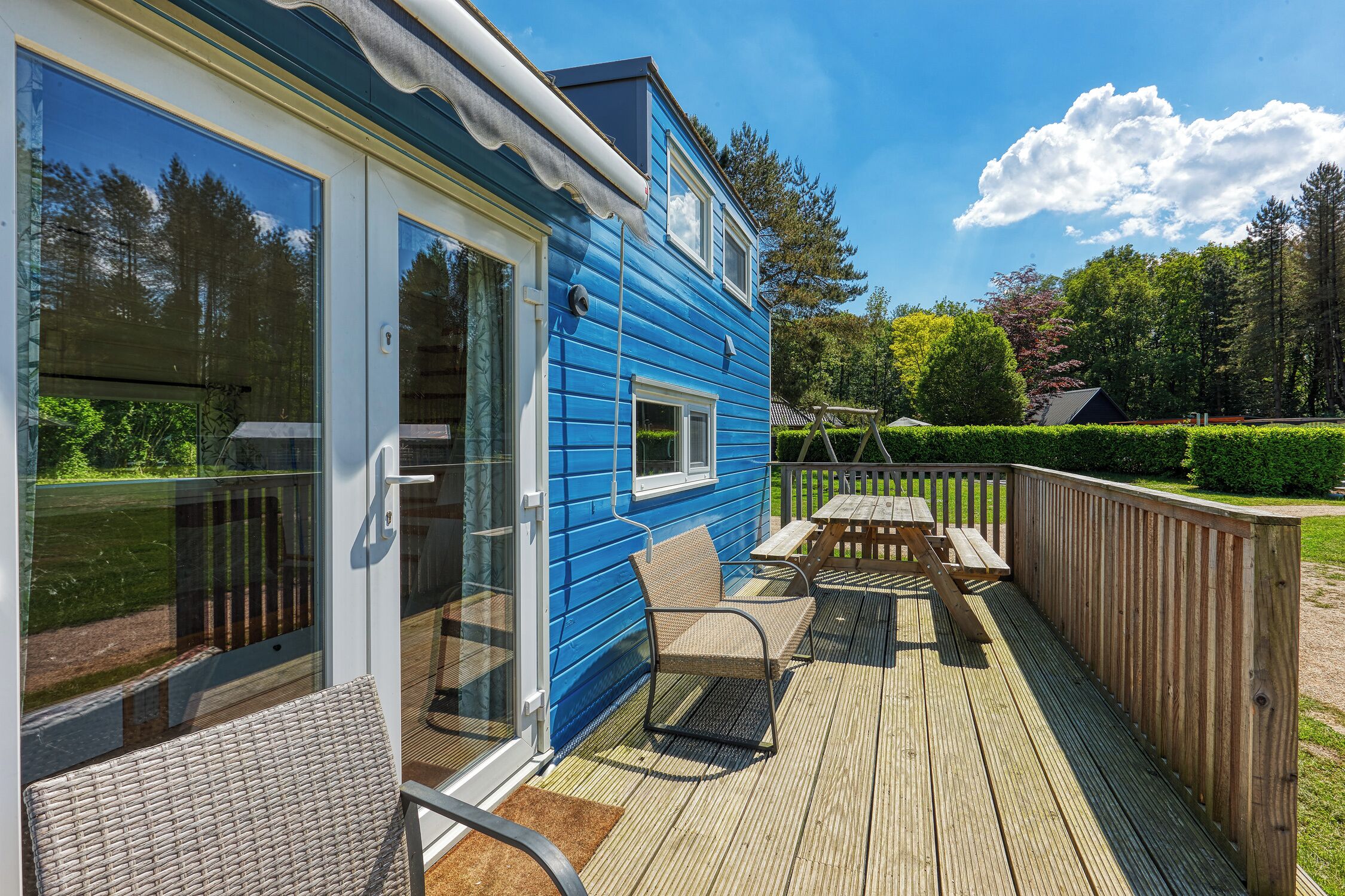 A blue house with a deck, a glass door, and a wooden table and chair.