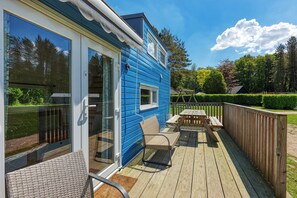 A blue house with a deck, a glass door, and a wooden table and chair.