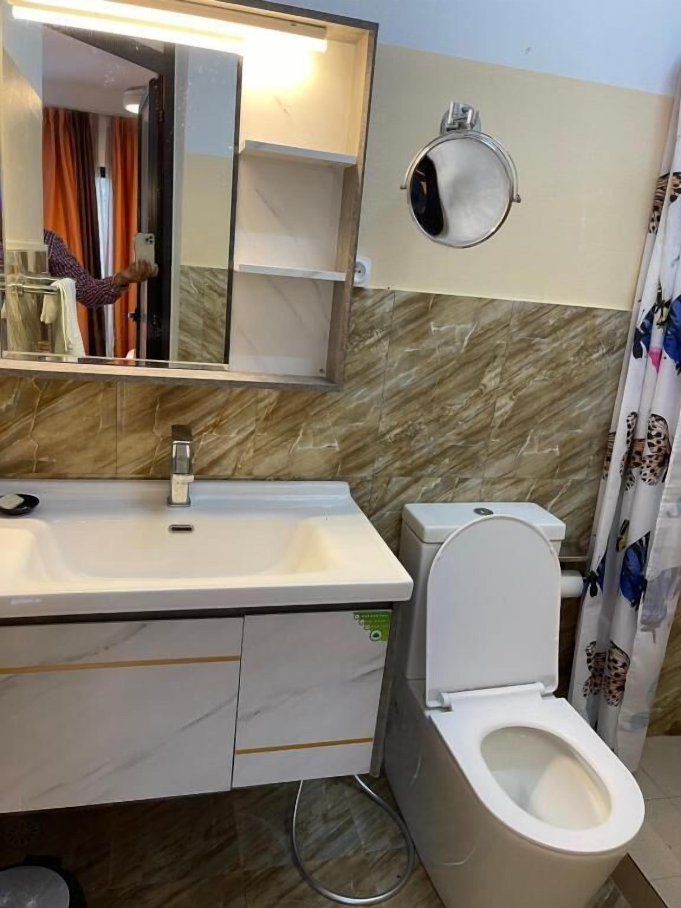 Une salle de bain avec un lavabo blanc, des toilettes, un miroir et un rideau de douche.