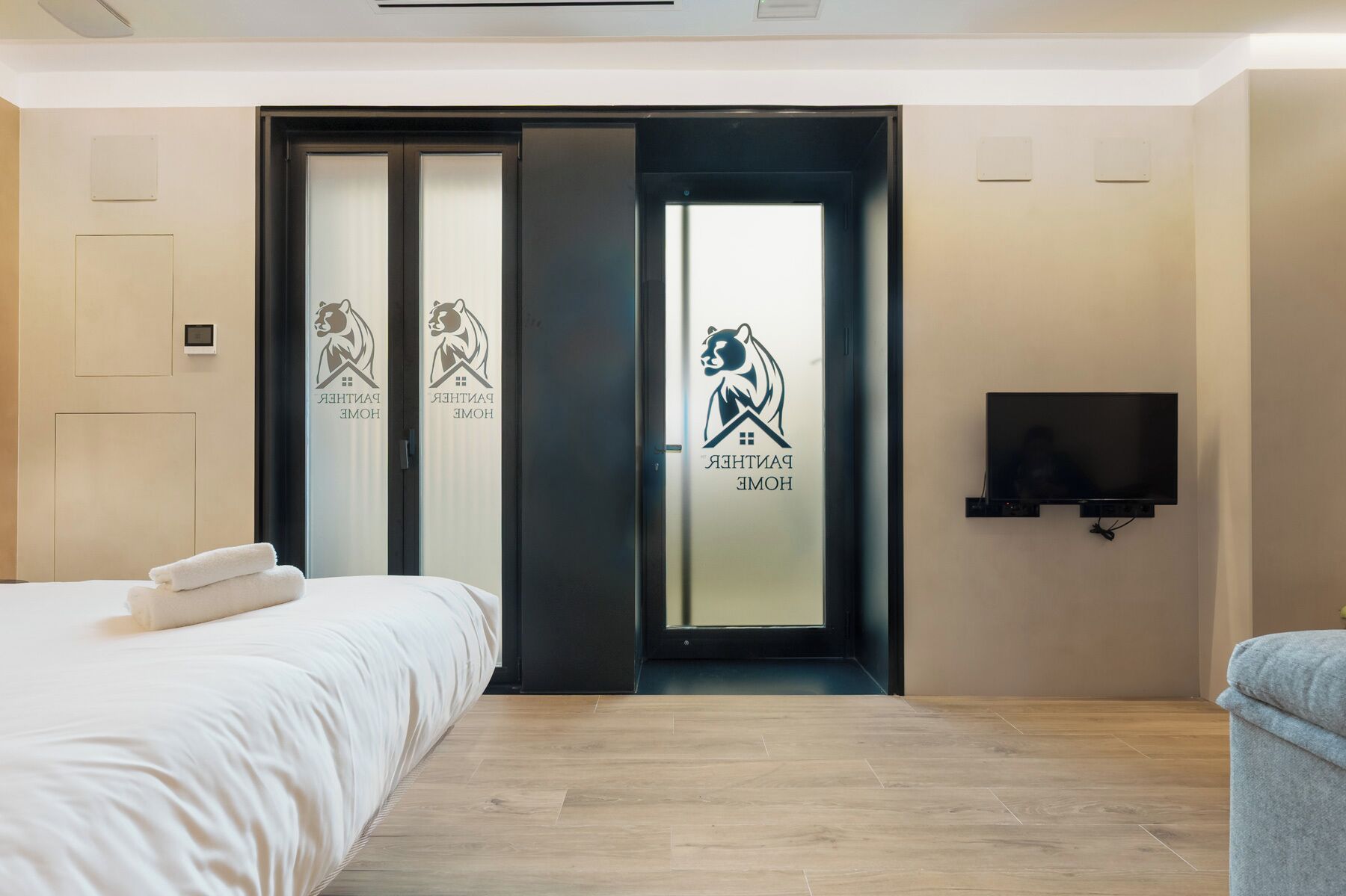 A hotel room with a bed, a TV, and a sliding door with a bear logo.