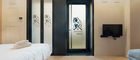 A hotel room with a bed, a TV, and a sliding door with a bear logo.