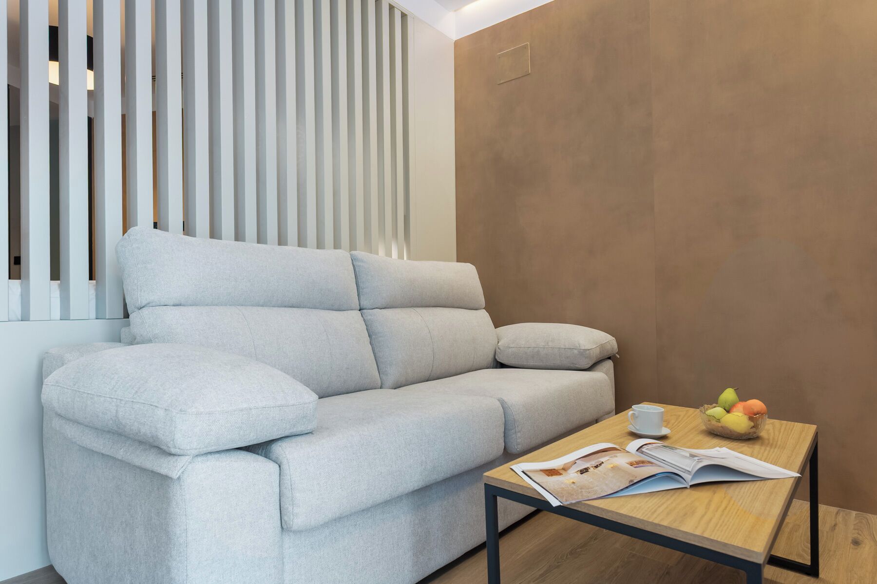Una sala moderna con un sofá gris, una mesa de centro de madera con una revista y un frutero.