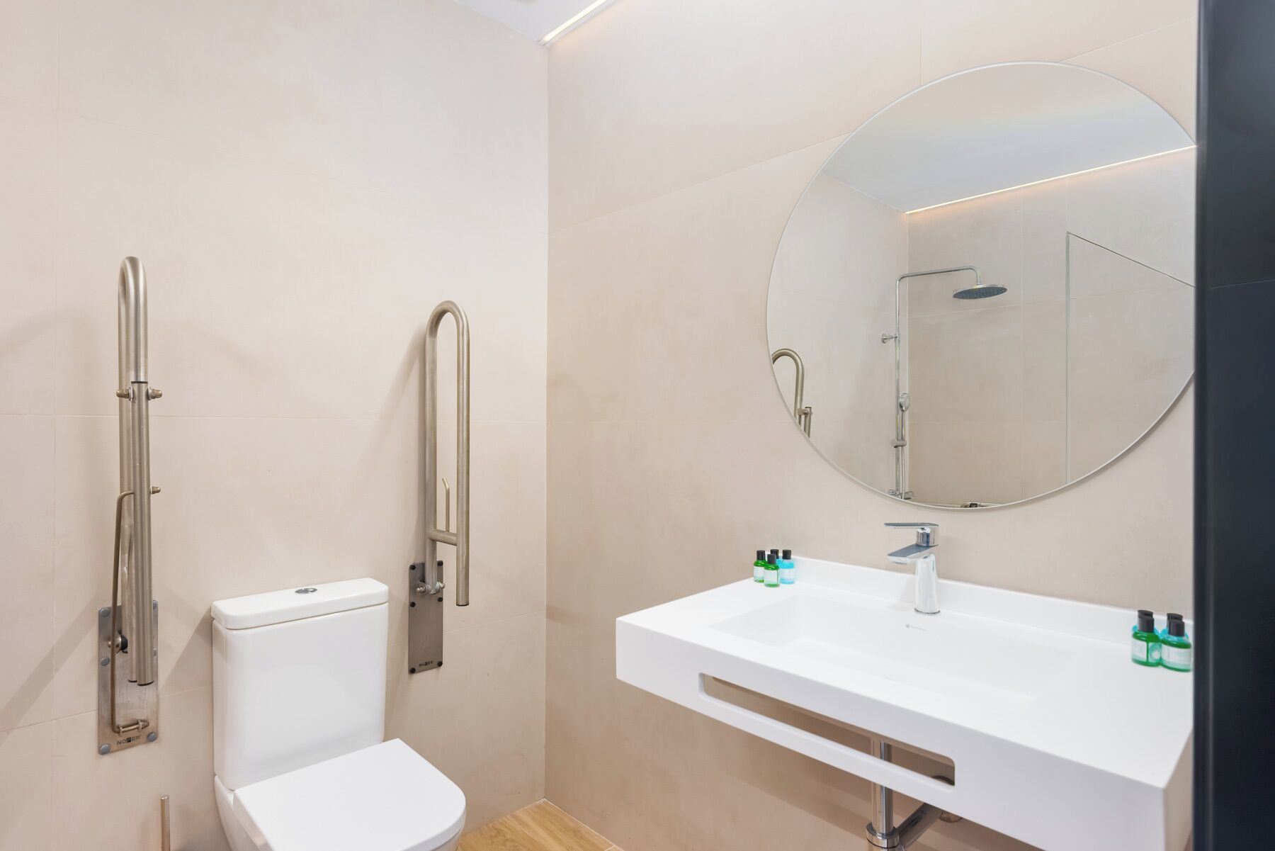 Un baño moderno con inodoro, ducha con barra de apoyo, lavamanos con espejo y artículos de aseo.