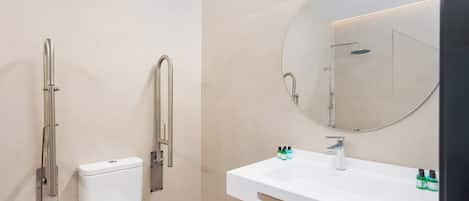 Un baño moderno con inodoro, ducha con barra de apoyo, lavamanos con espejo y artículos de aseo.