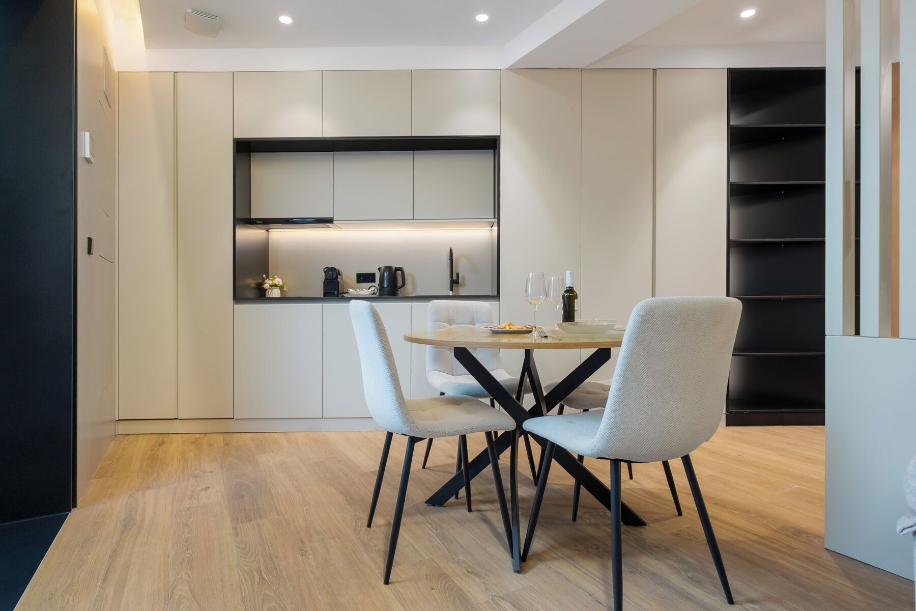 Una cocina moderna con electrodomésticos integrados, una mesa de comedor con sillas y una estantería.