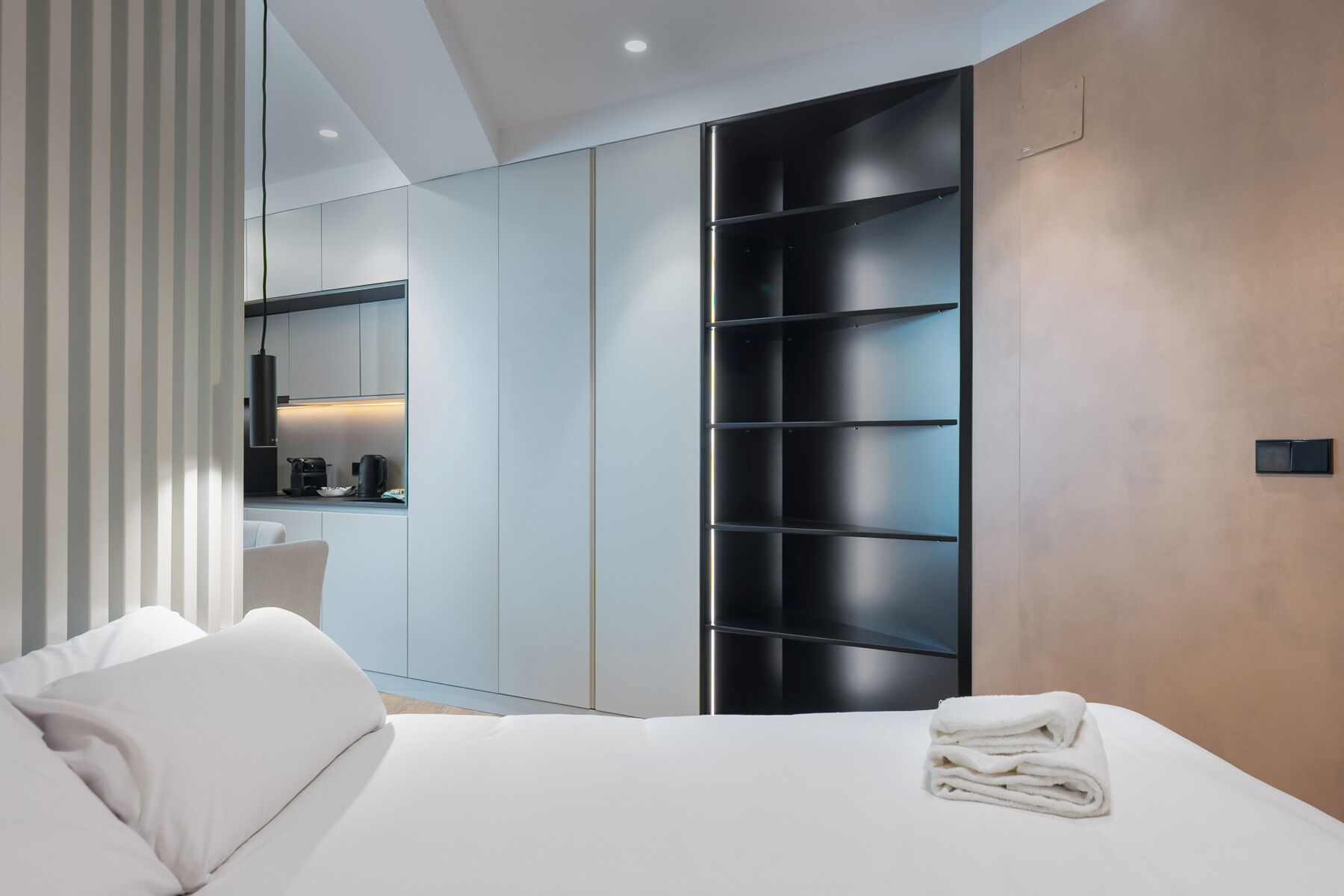 A modern bedroom with a bed, a bedside table, a wall-mounted shelf, and a built-in wardrobe.