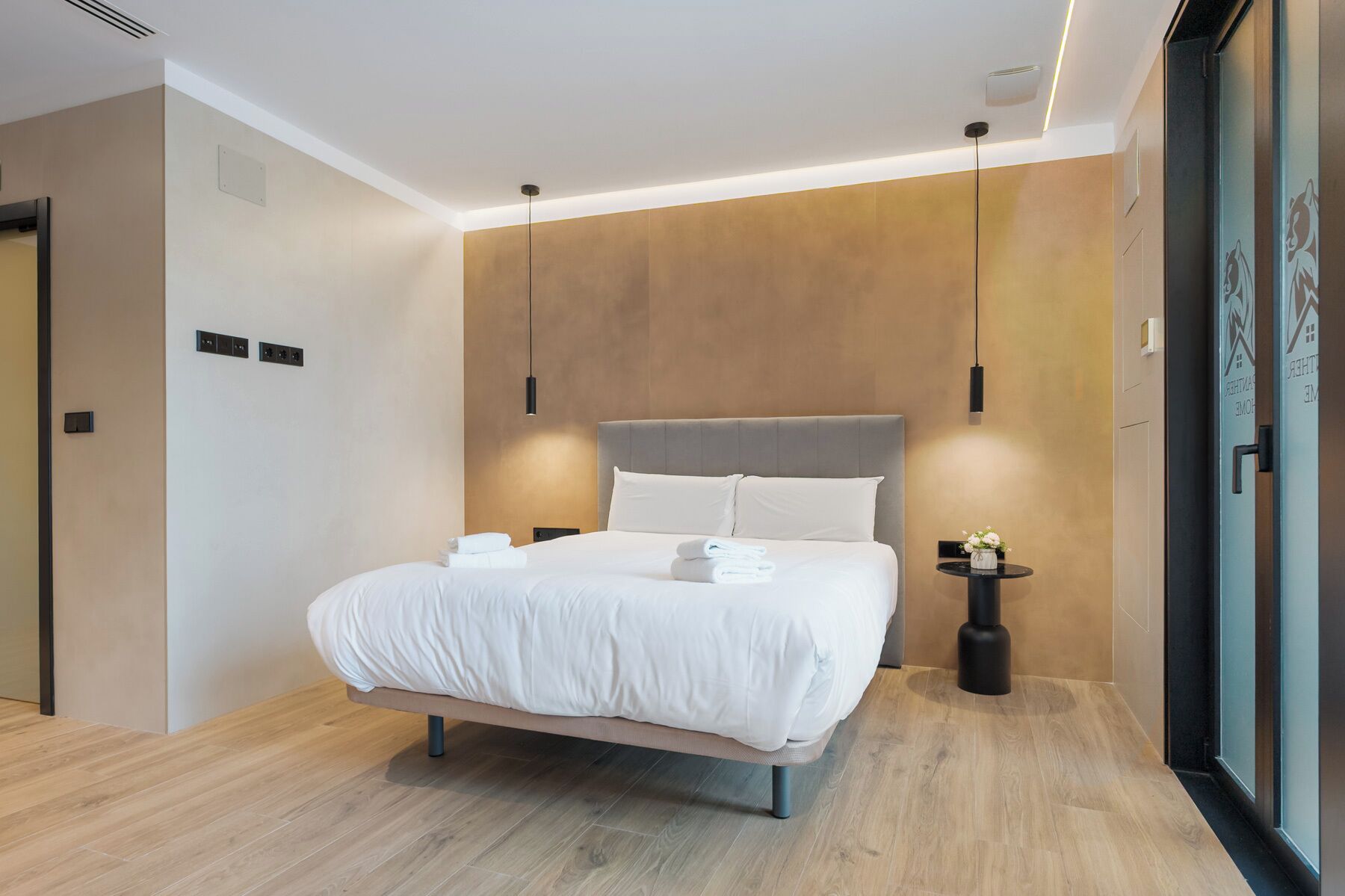 Una habitación de hotel moderna con una cama grande, una mesita de noche y una lámpara fijada a la pared.