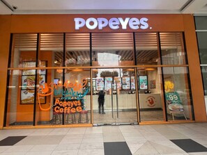 Um restaurante Popeyes com uma grande janela de vidro, um letreiro anunciando 'Popeyes Coffee' e um quadro de menu visível através da janela.