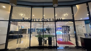 Der Eingang eines Hotels mit Glasfassade, einem Schild mit der Aufschrift "EIGHTY ONE MALL" und einem roten Teppich, der zum Innenbereich führt.