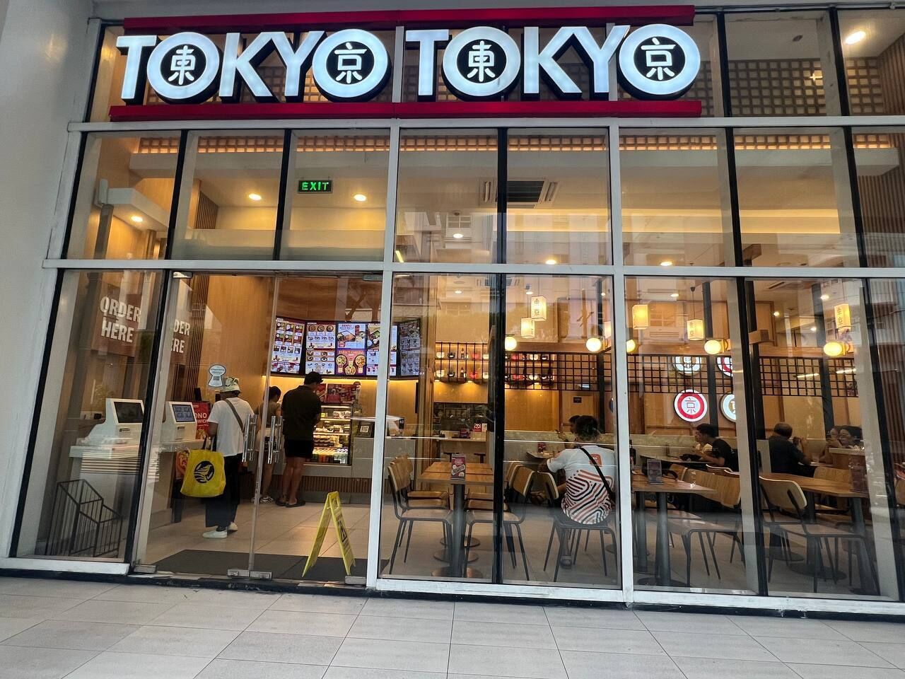 A Tokyo restaurant with a glass facade, indoor seating, and a visible menu board.