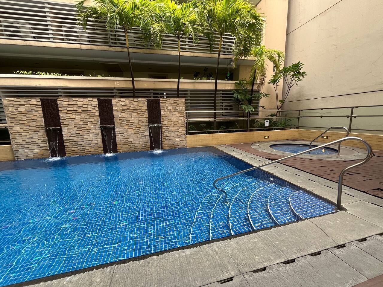 Una piscina con suelo de baldosas, rodeada por un muro de piedra y una barandilla de metal.