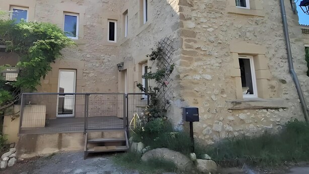 Un edificio in pietra con un cancello, delle scale che conducono a una porta e un piccolo giardino con rocce e piante.