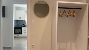 Een kamer met een witte inbouwkast, een ronde spiegel en een kapstok met hangers.