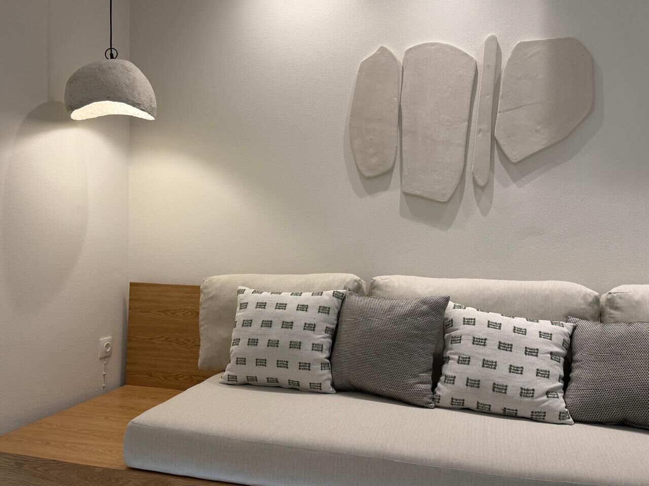 A modern living room with a sofa, patterned cushions, a hanging light fixture, and a wall-mounted abstract art piece.