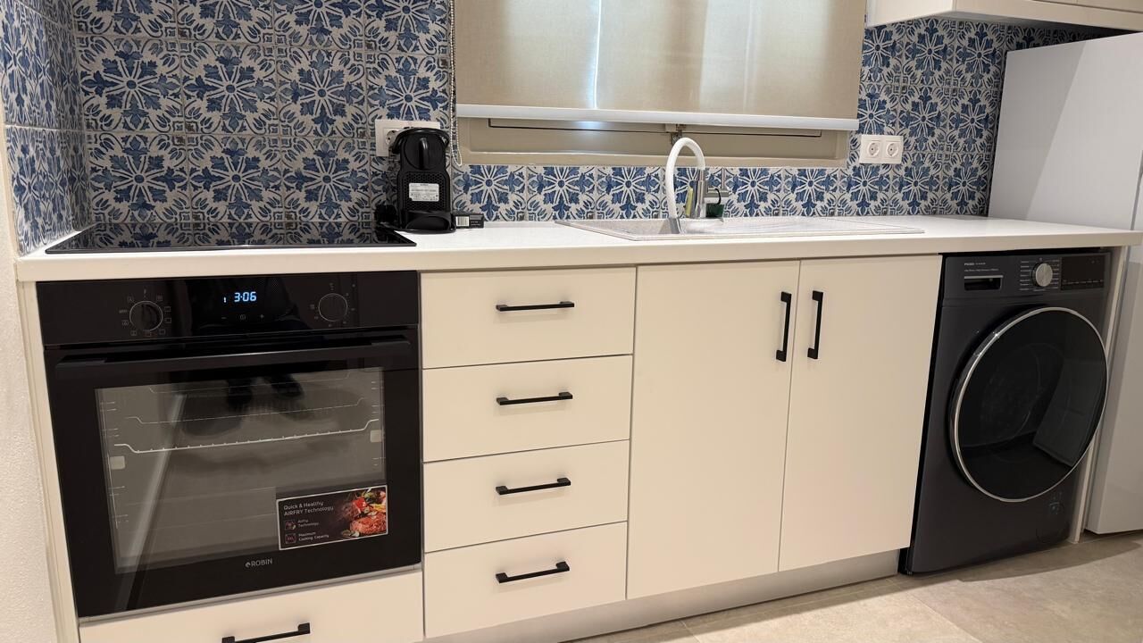 Una cocina equipada con horno empotrado, lavadora y cafetera.