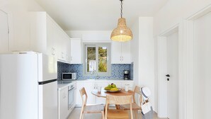Una cocina moderna con armarios blancos, salpicadero de azulejos azules, una mesa de comedor de madera con sillas y una lámpara colgante.