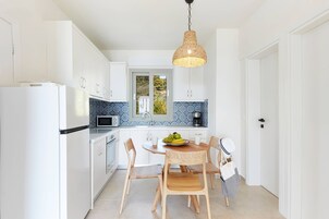 Una cocina moderna con armarios blancos, salpicadero de azulejos azules, una mesa de comedor de madera con sillas y una lámpara colgante.