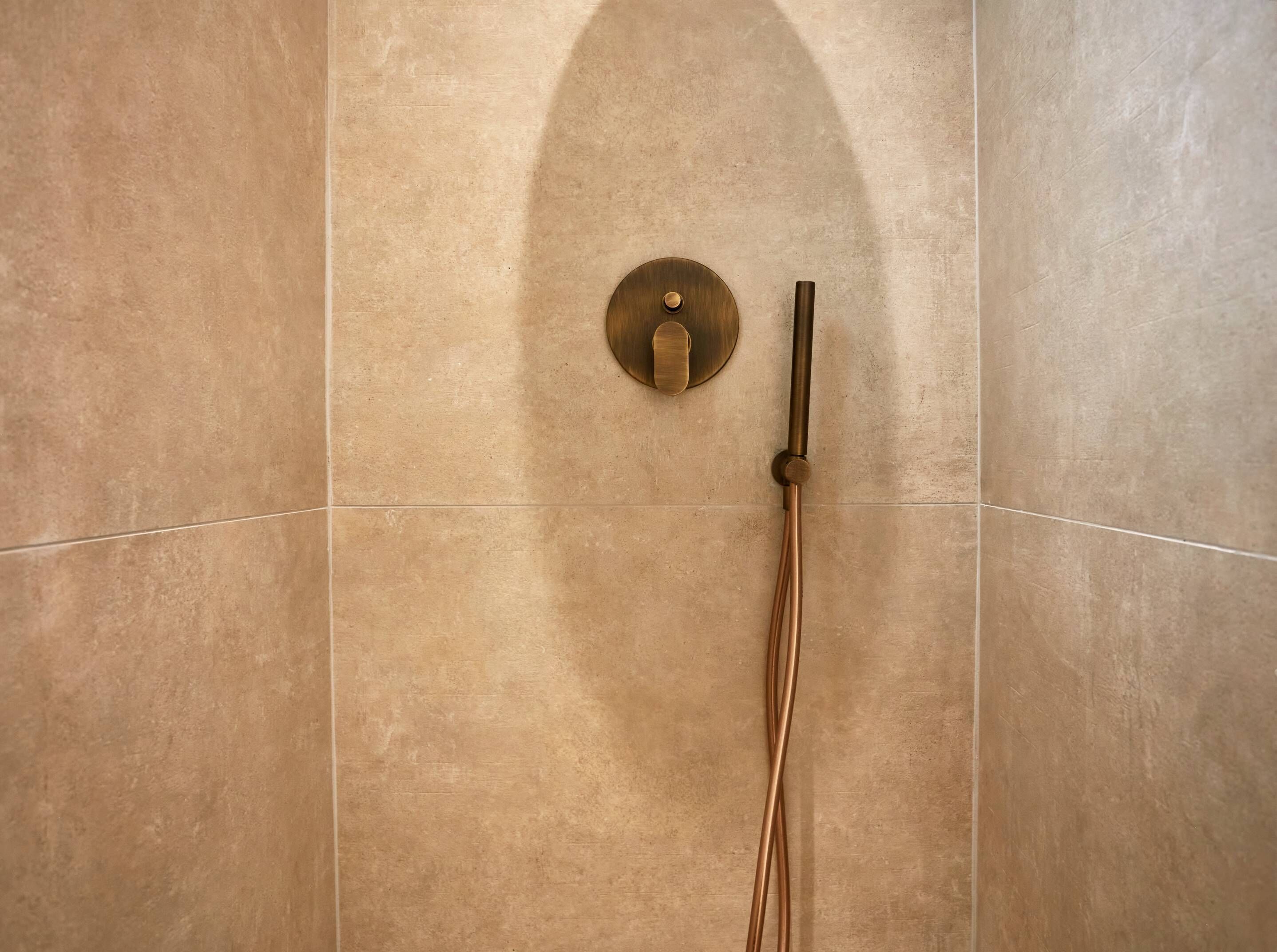 A shower with a single control knob and a handheld showerhead mounted on a wall with a textured tile surface.