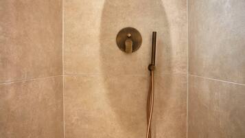 A shower with a single control knob and a handheld showerhead mounted on a wall with a textured tile surface.