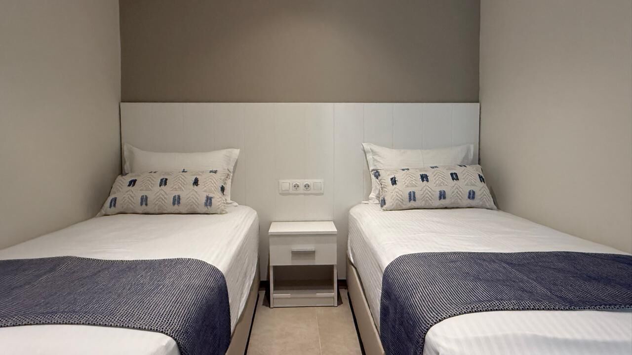 A twin room with two beds, a nightstand, and a wall-mounted outlet.