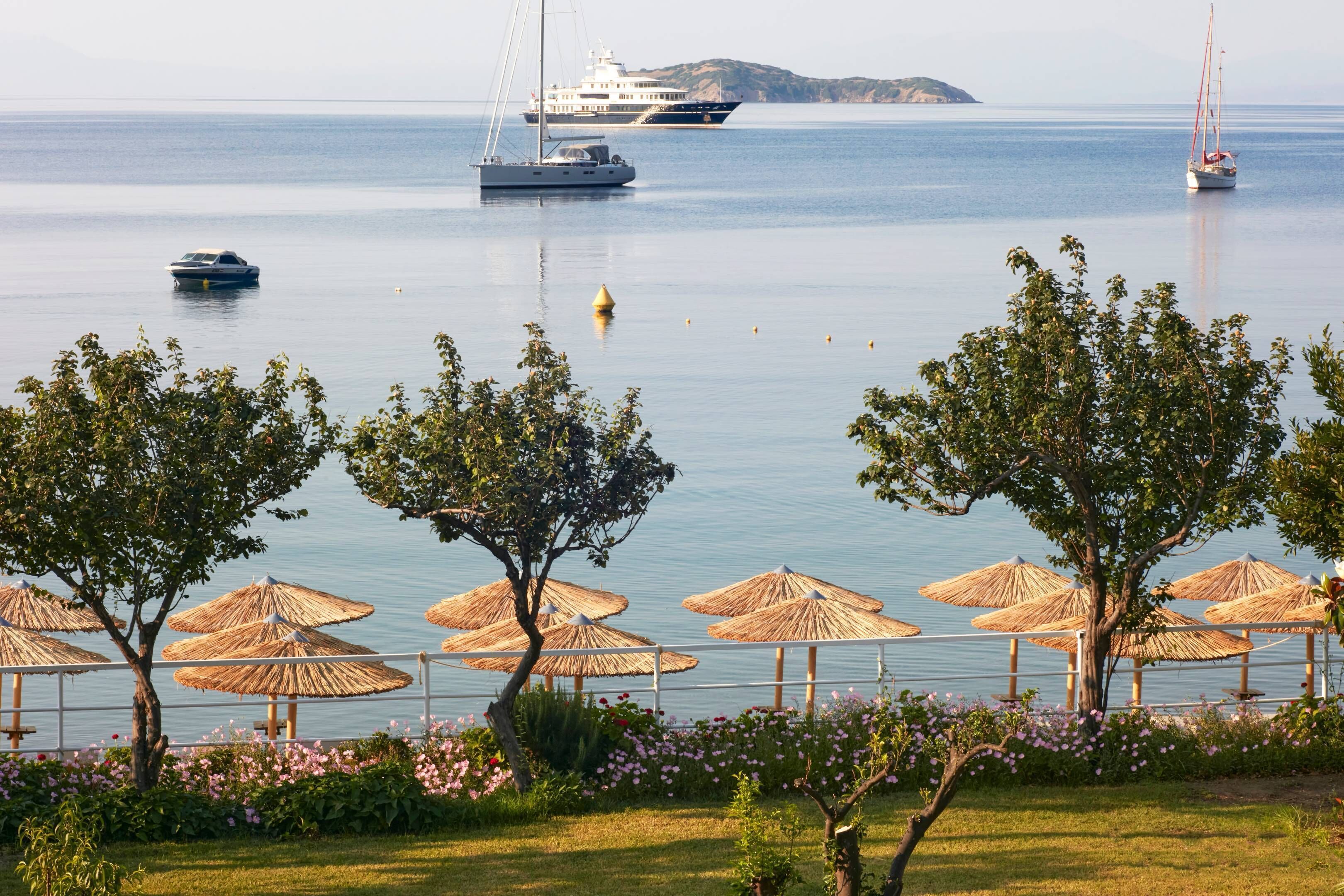 Vista costera con un puerto deportivo, barcos y una hilera de sombrillas de paja.
