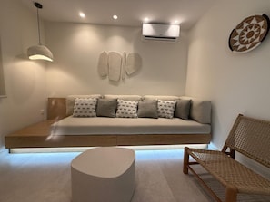 Een moderne woonkamer met een bank, een rond poef en een rieten fauteuil.