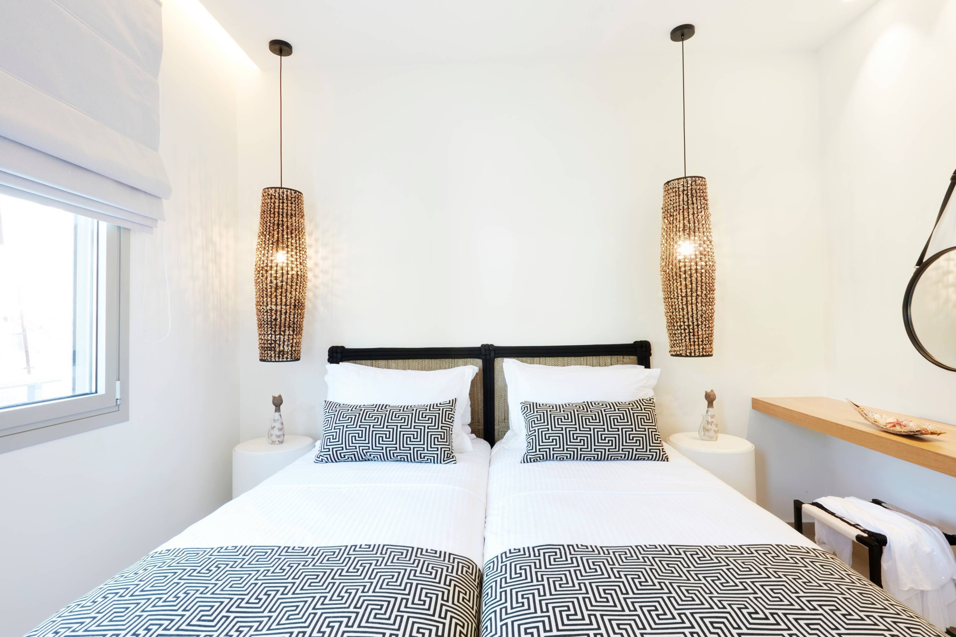 Una cama doble con estructura metálica negra, dos mesitas de noche, un ventanal y dos lámparas fijadas a la pared.