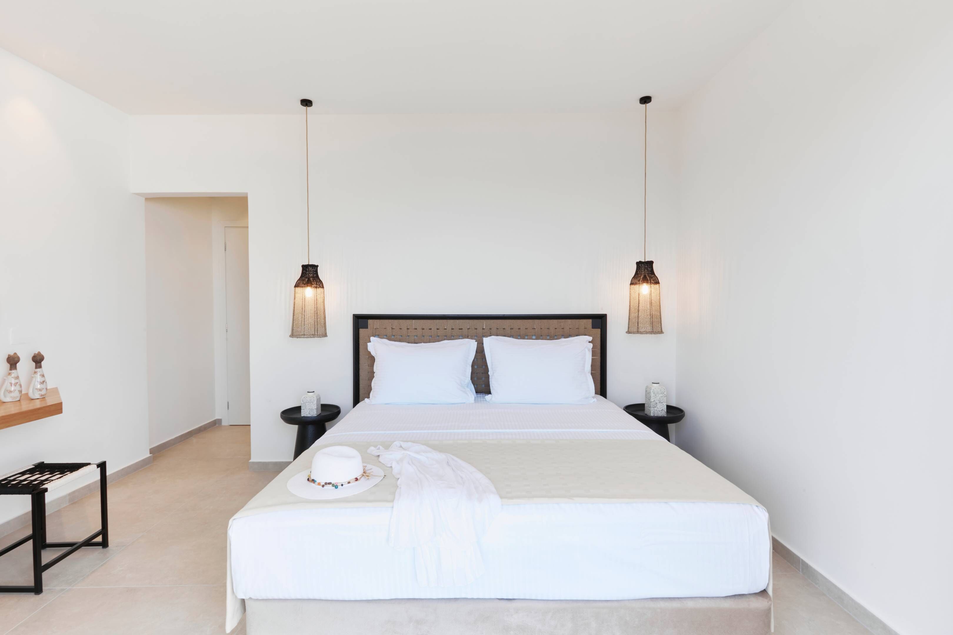 A hotel room with a bed, bedside tables, a nightstand, a small table with decorative items, and a bench.