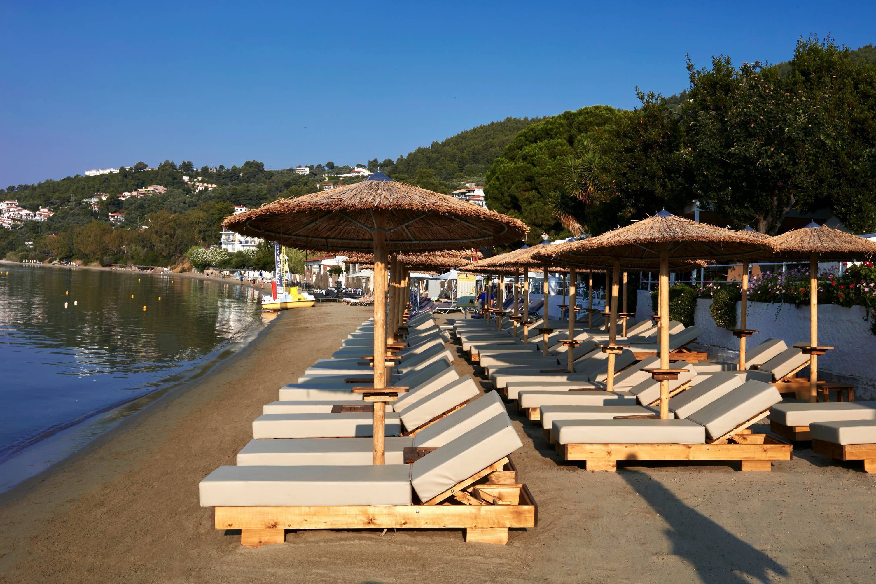 A beach with rows of sun loungers and thatched umbrellas.