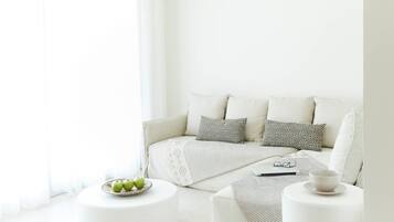 Una sala de estar moderna con un sofá blanco, almohadones estampados, una pequeña mesa redonda con un tazón de manzanas y una mesa de centro con una computadora portátil y vasos.