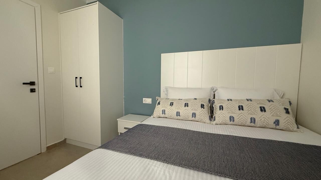 Un dormitorio con cama, mesita de noche, armario y pared azul.