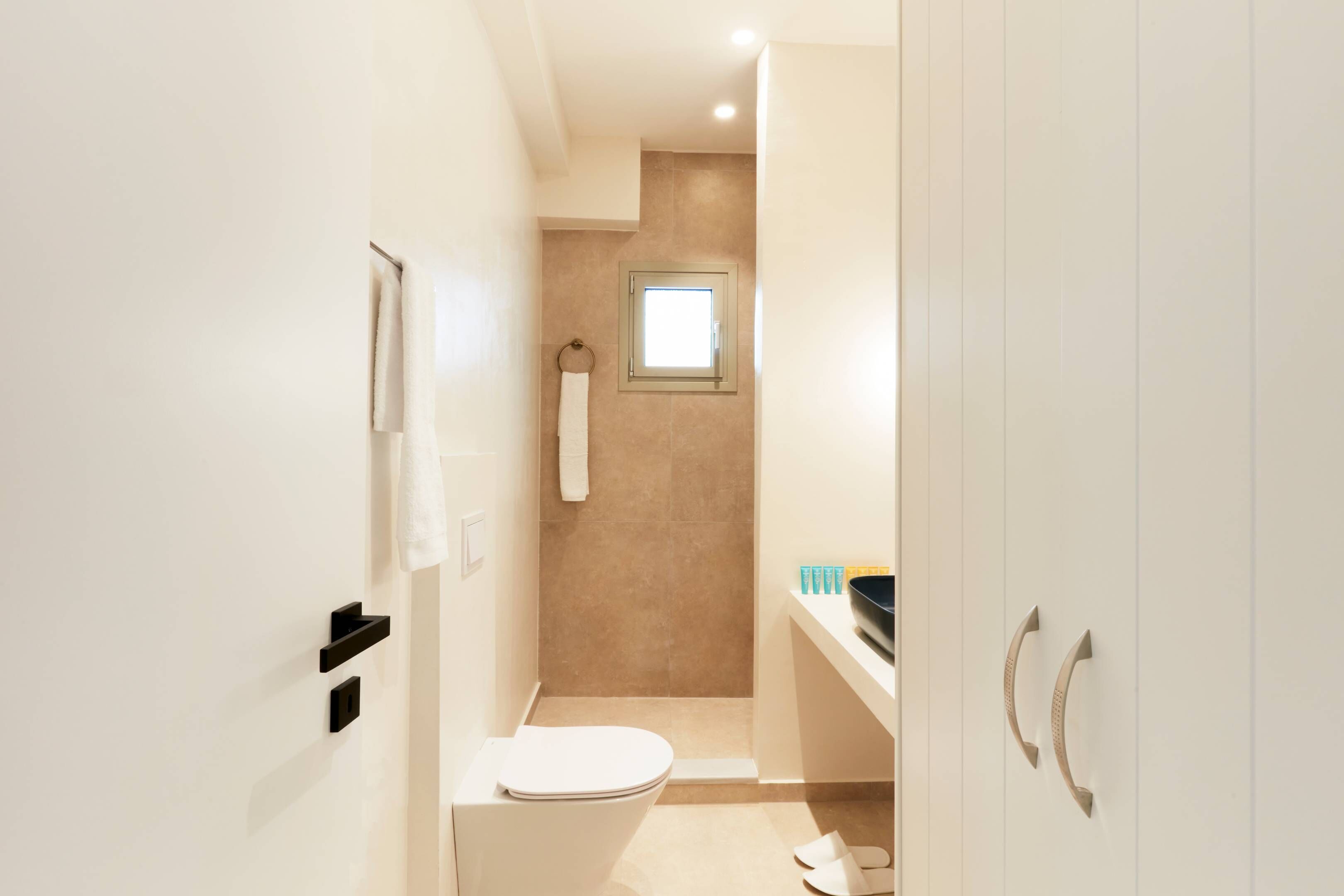 A narrow bathroom with a toilet, a towel rack, and a small window.