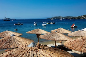 Una playa con sombrillas de paja y barcos en el agua.