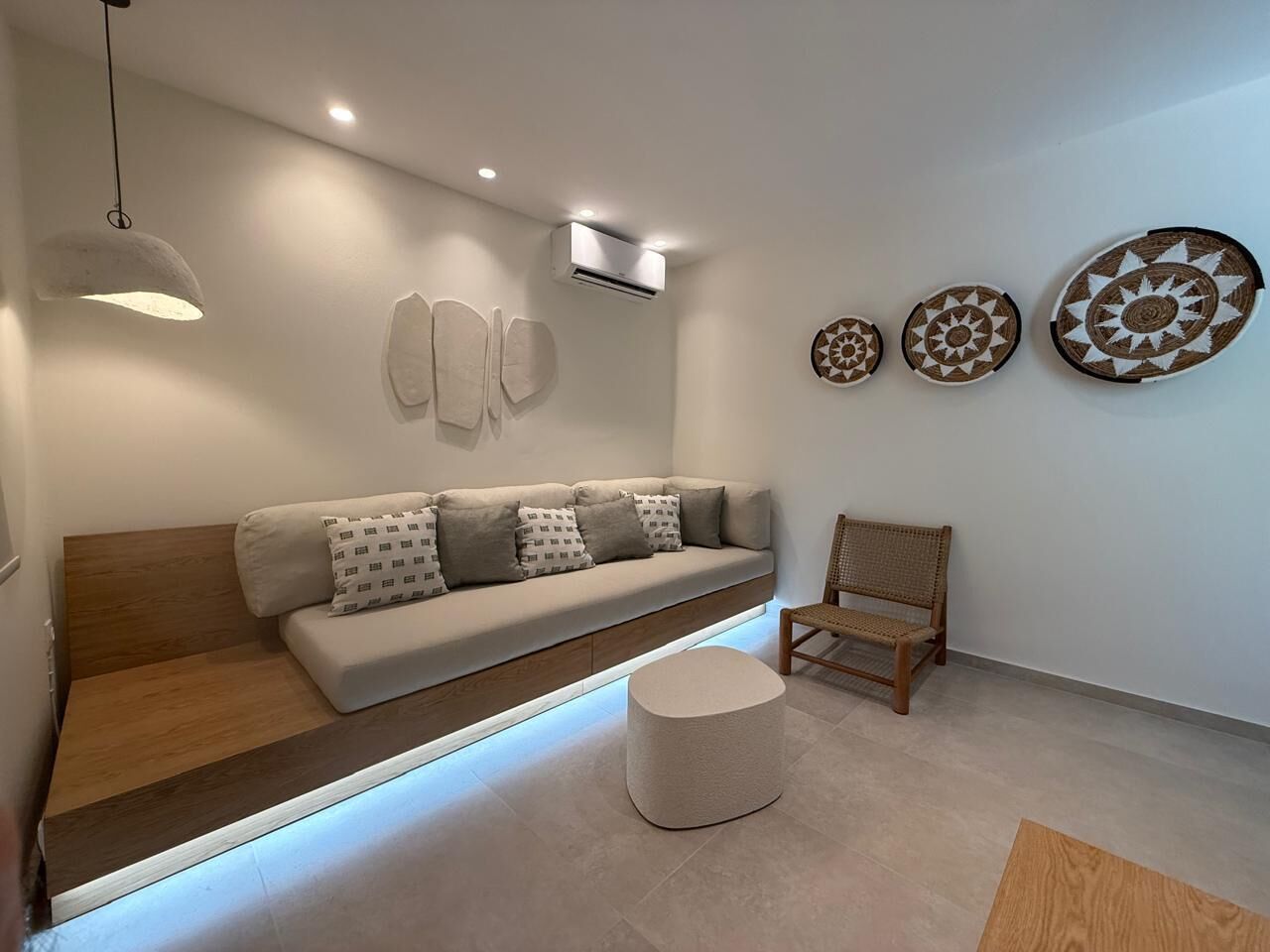 Ein stilvolles Wohnzimmer mit einer Couch, einem runden Hocker, einem Holzstuhl und Wandbildern.
