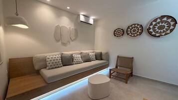 Ein stilvolles Wohnzimmer mit einer Couch, einem runden Hocker, einem Holzstuhl und Wandbildern.