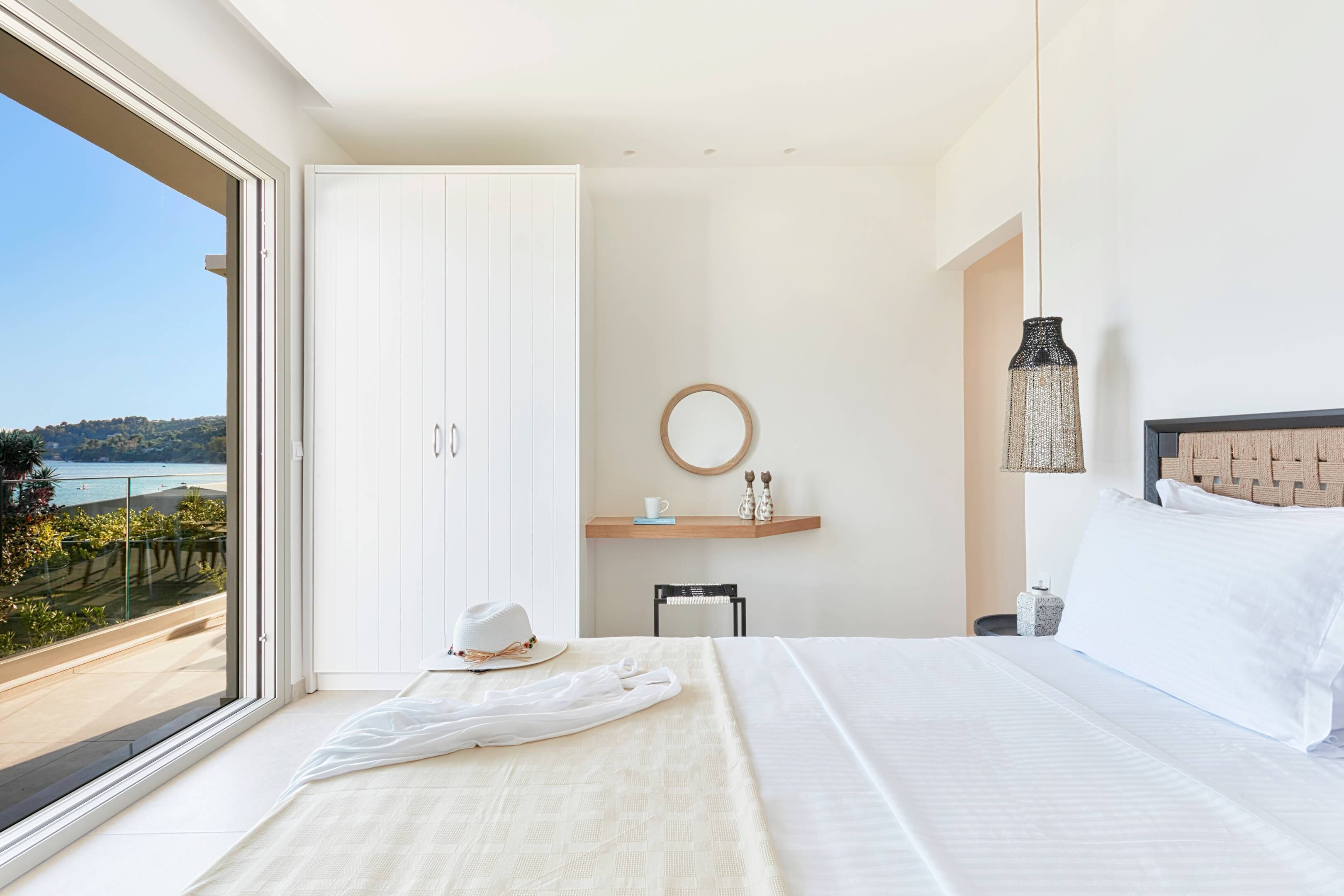 A bedroom with a large window, a bed, a bedside table, a chair, and a view of the outdoors.