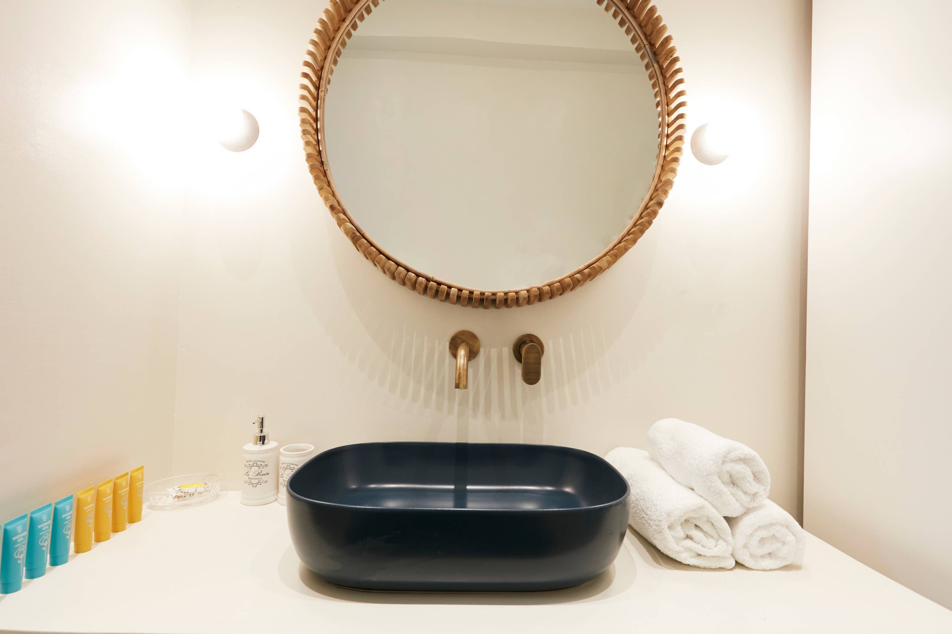 Ein Badezimmer mit einem schwarzen Waschbecken, einem Spiegel mit Holzrahmen, zwei Handtuchrollen und einer Reihe von Pflegeprodukten.