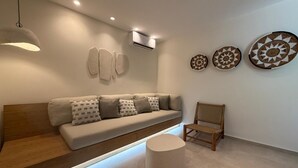 Una sala moderna con un sofá, un otoman redondos, una silla de madera y adornos en la pared.
